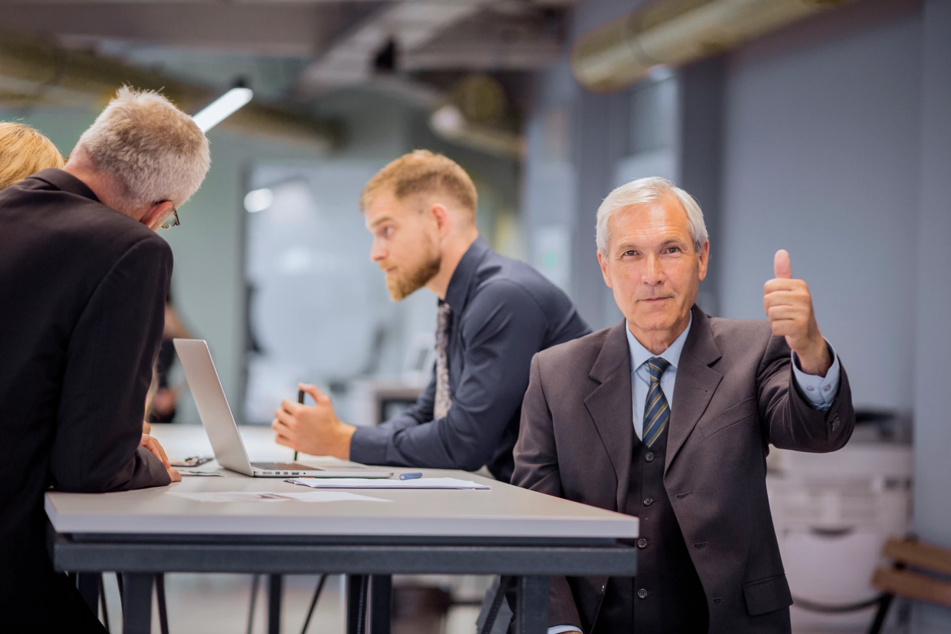 senior-businessman-showing-thumb-up-sign-sitting-front-his-team-discussing-office