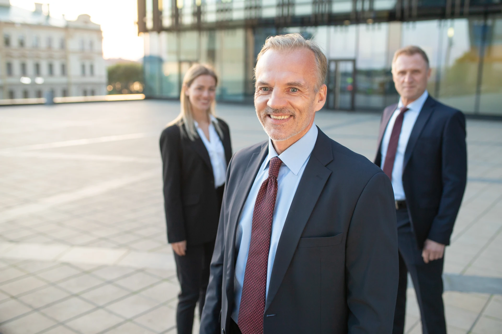 happy-middle-aged-businessman-wearing-office-suit-standing-outdoors-looking-camera-his-team-standing-teamwork-team-success-concept (1)